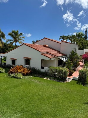 Ein eingeschossiges Haus mit rotem Ziegeldach, weißen Außenwänden und einem gepflegten Garten mit verschiedenen Pflanzen und Rasen.