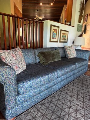 Ein blaues Sofa mit Muster, ein Teppich mit geometrischem Muster und Holzlatten im Hintergrund.