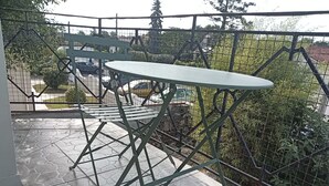 Un pati amb taula i cadires, un paviment de pedra i vistes a un carrer amb cotxes i vegetació.