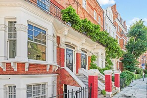 Une rangée de maisons de ville aux façades blanches et aux murs en briques rouges, un escalier menant à l’entrée et un ciel d’un bleu limpide.