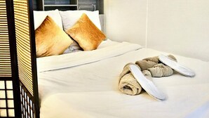 A neatly made bed with pillows and a rolled towel, a bedside table with a lamp, and a wall-mounted light fixture. - Hana House - Zen journey in the heart of Paris (Paris)