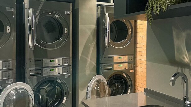 Een moderne wasruimte met gestapelde wasmachines en drogers, een wasbak en een accentmuur van baksteen.
