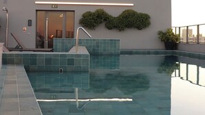 Een dakzwembad met een helder uitzicht op de stadshemel, een moderne gevel en een klein inkomgedeelte met een deur en een trap.