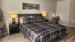 A neatly arranged bedroom with a bed, two bedside tables with lamps, a ceiling fan, and a cityscape painting on the wall. - Modern Stay Near Fort Sill + Park & Shopping (Lawton)