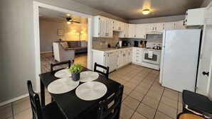 A modern kitchen with white cabinets, a black dining table with placemats, and a white refrigerator. - Modern Stay Near Fort Sill + Park & Shopping (Lawton)