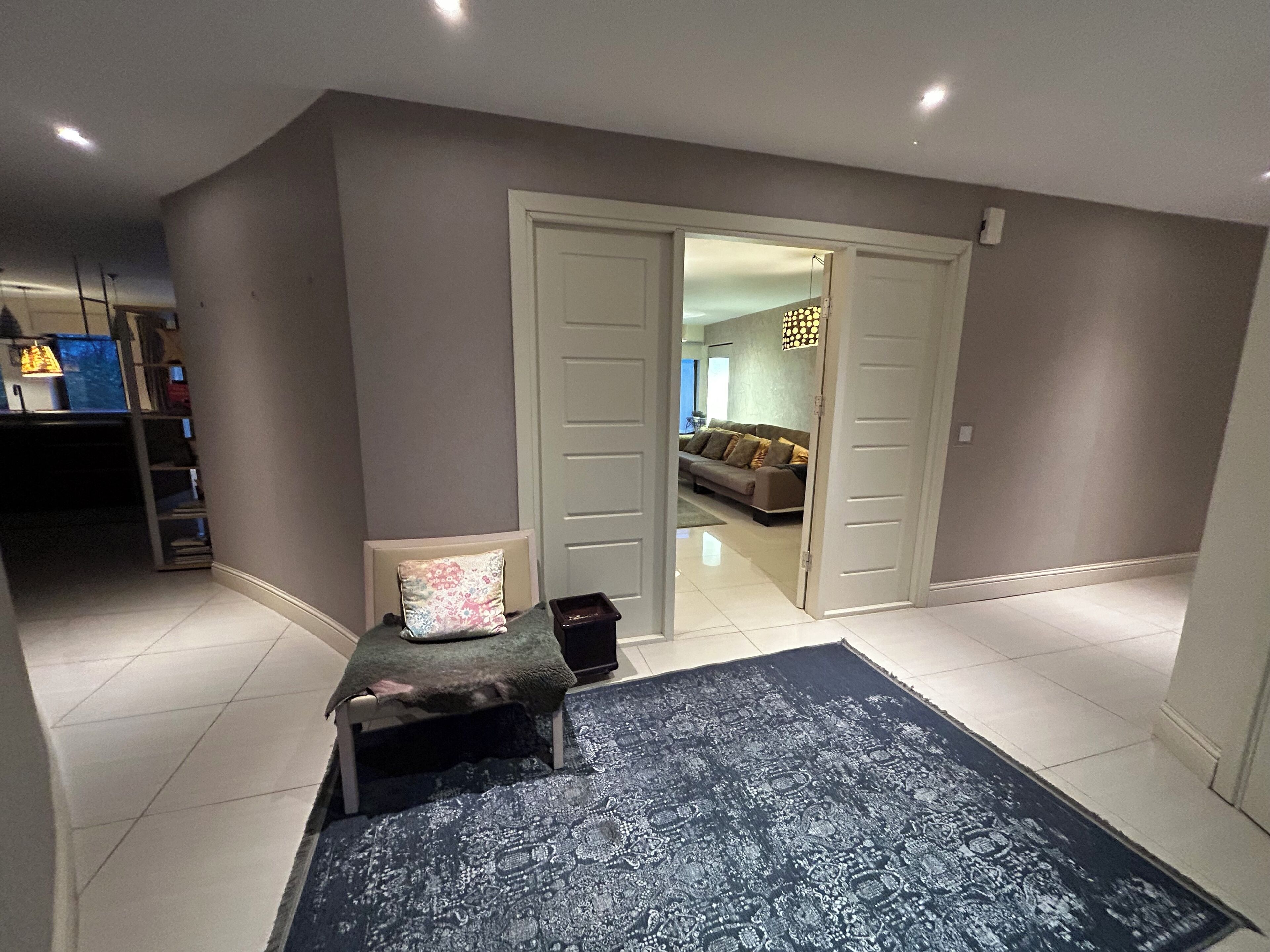Una habitación con un tapete de diseño oscuro, un banco con cojines y una puerta que da a otra habitación con un sofá y una lámpara.