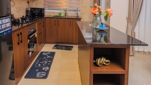 A modern kitchen with wooden cabinets, a black countertop, and a built-in oven. There is a small shelf with decorative items and a vase with flowers on the countertop. - Amazing Pool View Apartment  perfect in Garuga-Entebbe with fitness room & WI-FI (Nkumba)