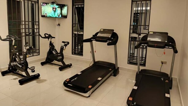 A home gym with treadmills, stationary bikes, and a TV mounted on the wall. - Amazing Pool View Apartment  perfect in Garuga-Entebbe with fitness room & WI-FI (Nkumba)