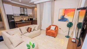 A living room with a beige sectional sofa, an orange armchair, a wooden coffee table, and a green floor lamp. - Amazing Pool View Apartment  perfect in Garuga-Entebbe with fitness room & WI-FI (Nkumba)