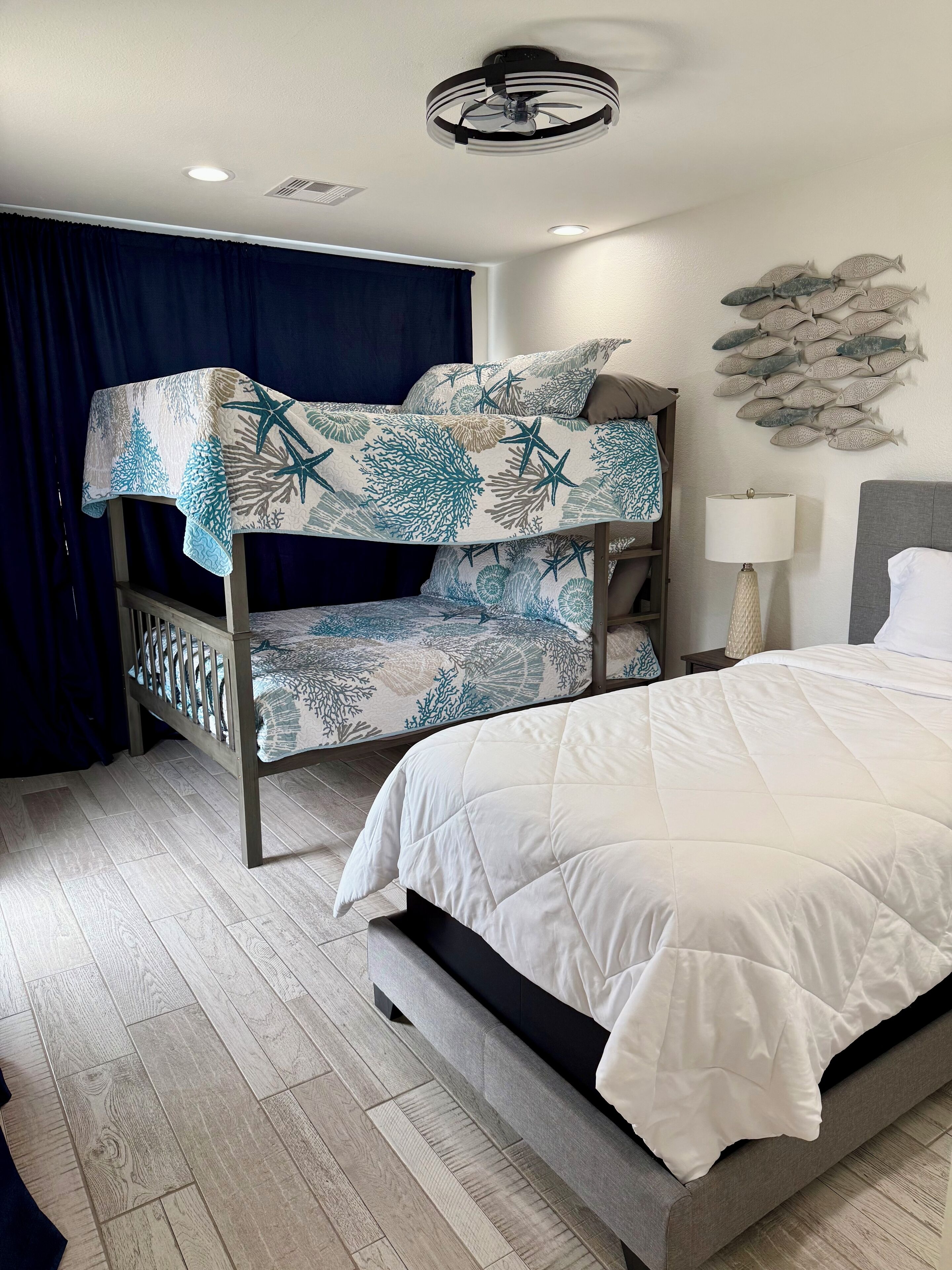 A bunk bed with a nautical-themed bedspread, a bedside lamp, and a wall decoration of fish.