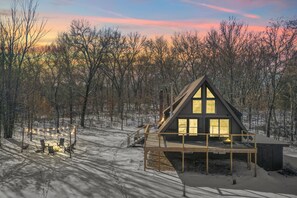 A cabin with a deck, surrounded by trees, during sunset. - Cozy Secluded A-Frame Cabin with Hot Tub & Fire Pit Near Dells & Mauston (Mauston)