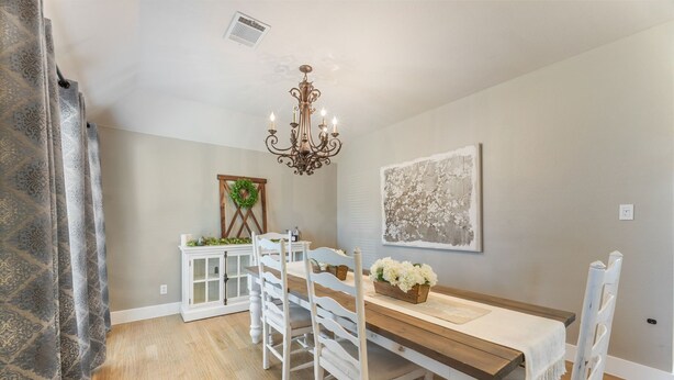 Une salle à manger avec une table en bois, des chaises blanches, un lustre et une œuvre d’art encadrée accrochée au mur.