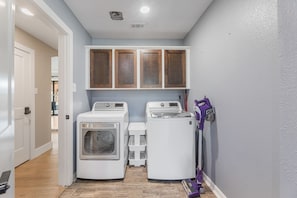A laundry room with two washing machines, a dryer, and a purple vacuum cleaner.