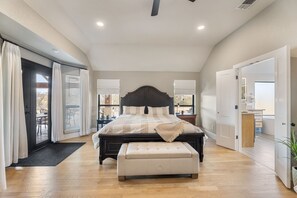 A bedroom with a large bed, a bench, a sliding glass door, and a desk.