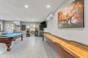 A pool table, a shuffleboard table, and a large abstract painting on a wall.