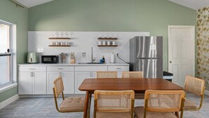 A compact kitchen with white cabinets, a stainless steel refrigerator, and a dining area with a wooden table and wicker chairs. - Sunny Auburndale Retreat w/ Pool (Auburndale)