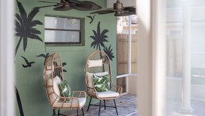 A room with two wicker chairs, a ceiling fan, and a wall painted in green with palm tree and bird murals. - Sunny Auburndale Retreat w/ Pool (Auburndale)