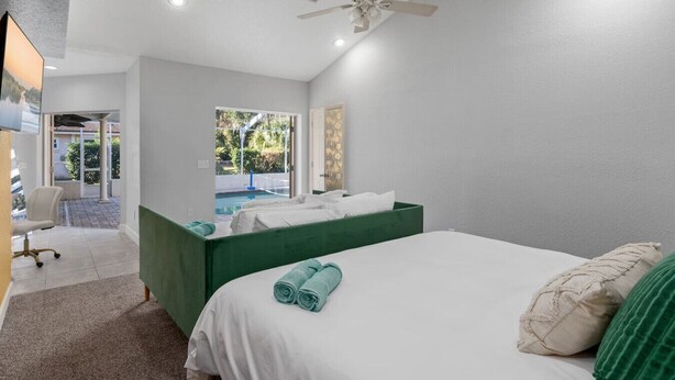 A modern hotel room with a bed, a desk, a chair, a green bench, and a view of a swimming pool. - Sunny Auburndale Retreat w/ Pool (Auburndale)