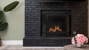 A fireplace with a visible fire, a brick wall, and a plant to the left.
