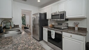 A modern kitchen with white cabinets, stainless steel appliances, granite countertops, and a built-in oven.