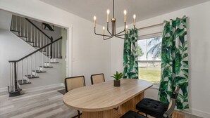 A dining area with a wooden table, black chairs, a chandelier, and tropical curtains.