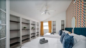 A hotel room with two beds, a ceiling fan, a wardrobe with shelves, and a patterned wall.
