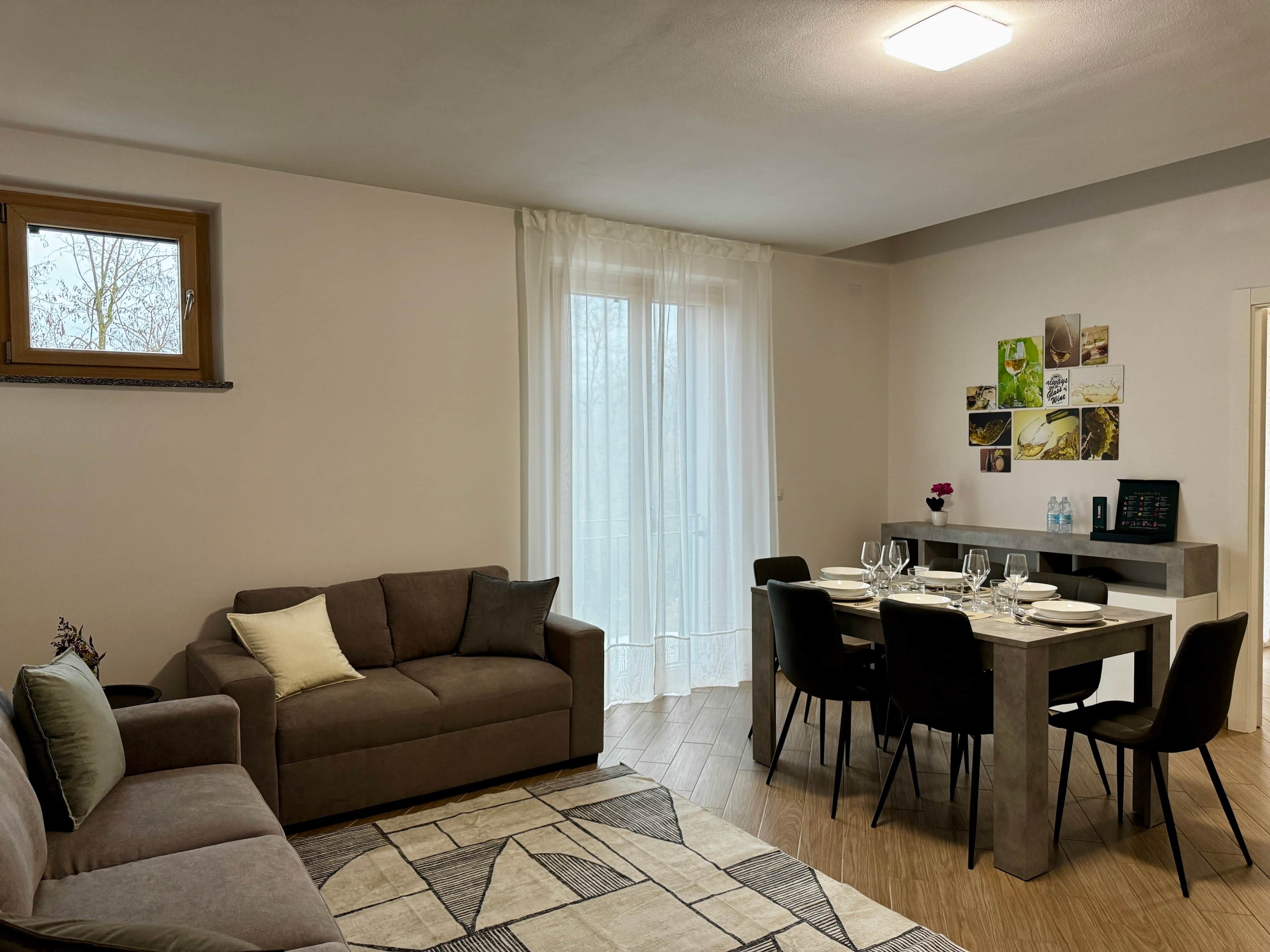 Un salon moderne avec un canapé marron, une table à manger entourée de chaises et une grande fenêtre ornée de rideaux légers.