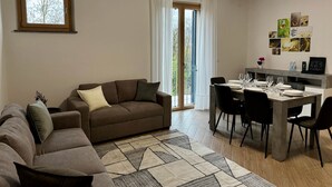 Ein Wohnzimmer mit braunem Sofa, einem Esstisch mit Stühlen und Blick durch eine Glastür nach draußen.