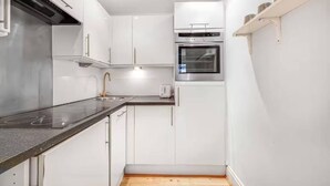 Cucina compatta con mobili bianchi, forno in acciaio inossidabile e piano di lavoro nero.