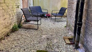 Una piccola area esterna con sedute, due sedie e un tavolo, circondata da un muro in mattoni e un fondo in ghiaia.