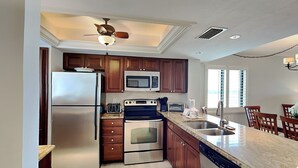 A modern kitchen with stainless steel appliances, wooden cabinets, and a granite countertop. - Carlos Pointe 611 (Fort Myers Beach)