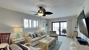 A spacious living room with a ceiling fan, a sofa with multiple cushions, a coffee table, a TV, and a balcony with outdoor seating. - Carlos Pointe 611 (Fort Myers Beach)