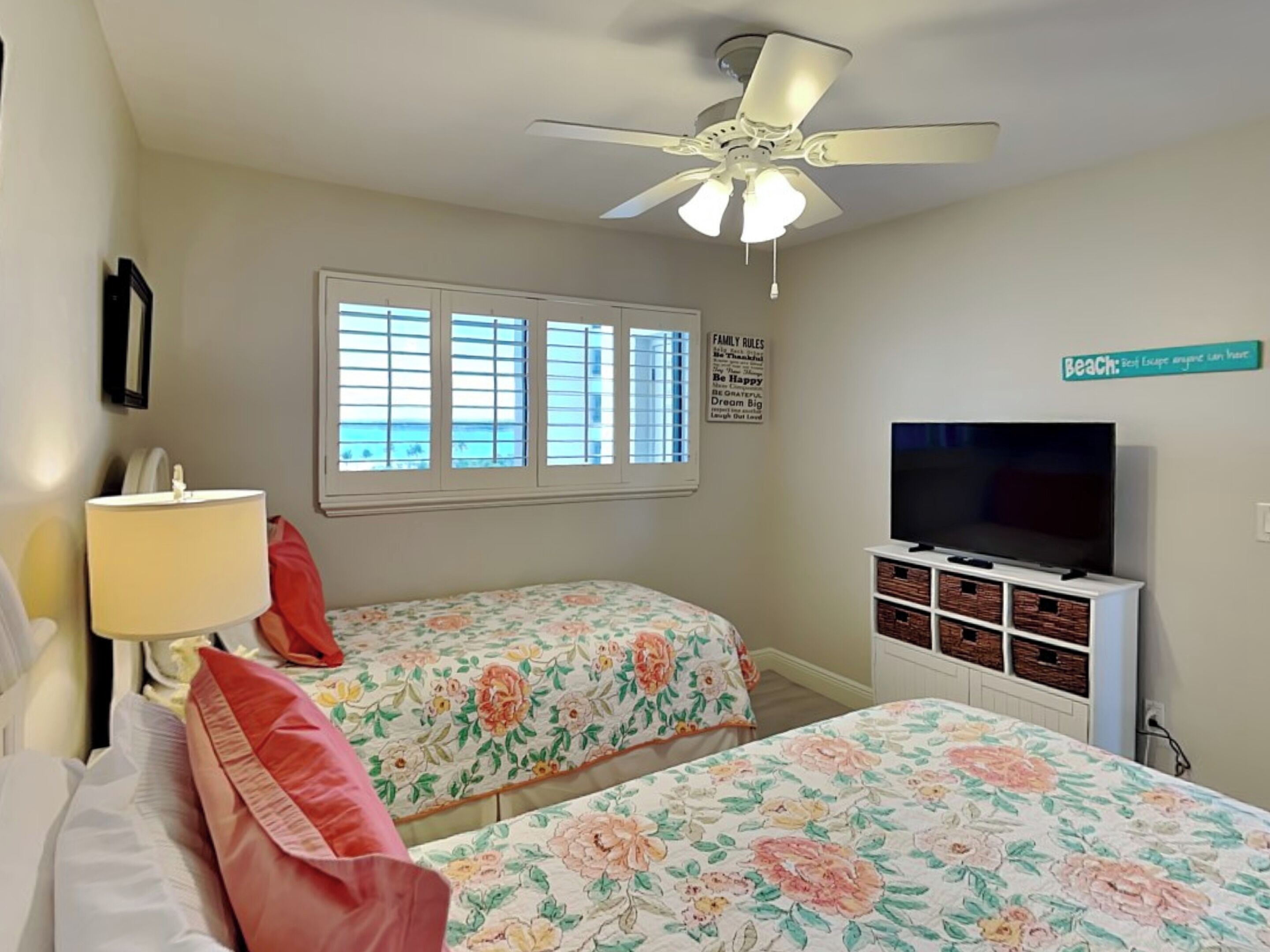 A bedroom with two beds, a ceiling fan, a TV, and a window with blinds.