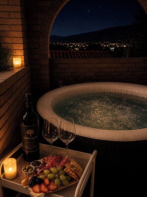 Un bain à remous avec vue sur la ville, éclairé la nuit, une bougie, une bouteille de vin et un plateau avec de la nourriture et des boissons.