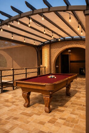 Een pooltafel met ballen, een bakstenen muur en een pergola met verlichting.