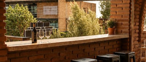A bar area with a brick wall, wooden ceiling beams, and a view of a building with a billboard.