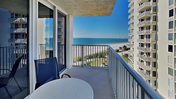 Un balcone con un tavolo e sedie bianche, vista su una spiaggia e un grattacielo.