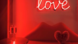A room with a neon 'love' sign, a round table with two glasses, and a sofa with a heart-shaped pillow. - Private Romantic Retreat for Two • Luxury Escape (Chicago)