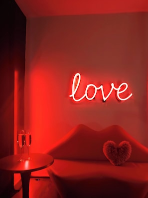 A room with a neon 'love' sign, a round table with two glasses, and a sofa with a heart-shaped pillow. - Private Romantic Retreat for Two • Luxury Escape (Chicago)