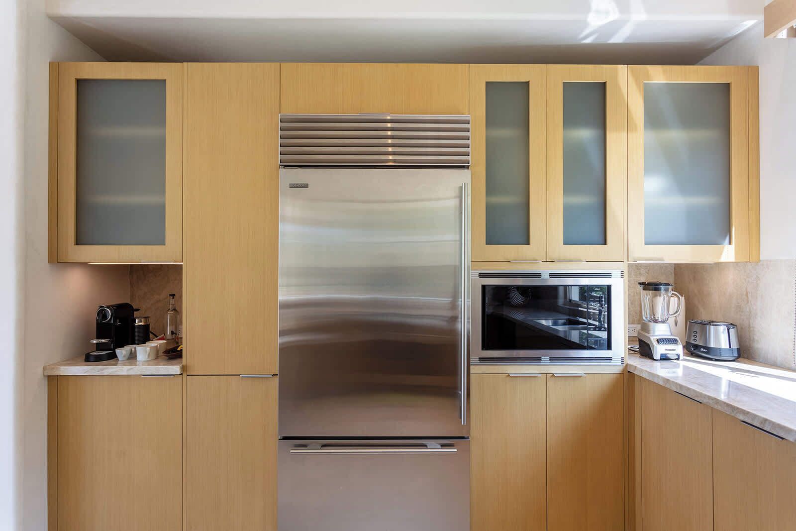 Een moderne keuken met houten kastjes, een roestvrijstalen koelkast, een inbouwoven en een koffiezetapparaat.