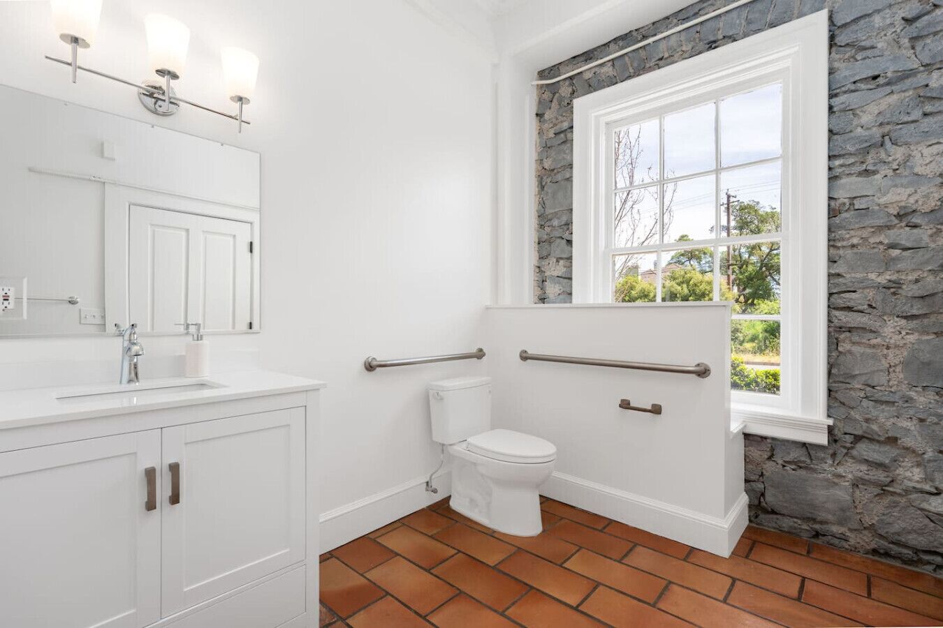 Un bagno con un mobile lavabo bianco, un water e una finestra con pareti in pietra.