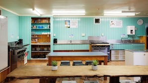 A kitchen with teal walls, stainless steel appliances, and a wooden table with potted plants. - Pacific Coast Lodge and Backpackers (Tauranga)