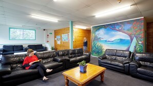 A waiting area with leather sofas, a wooden coffee table, and a mural of a tropical scene. - Pacific Coast Lodge and Backpackers (Tauranga)