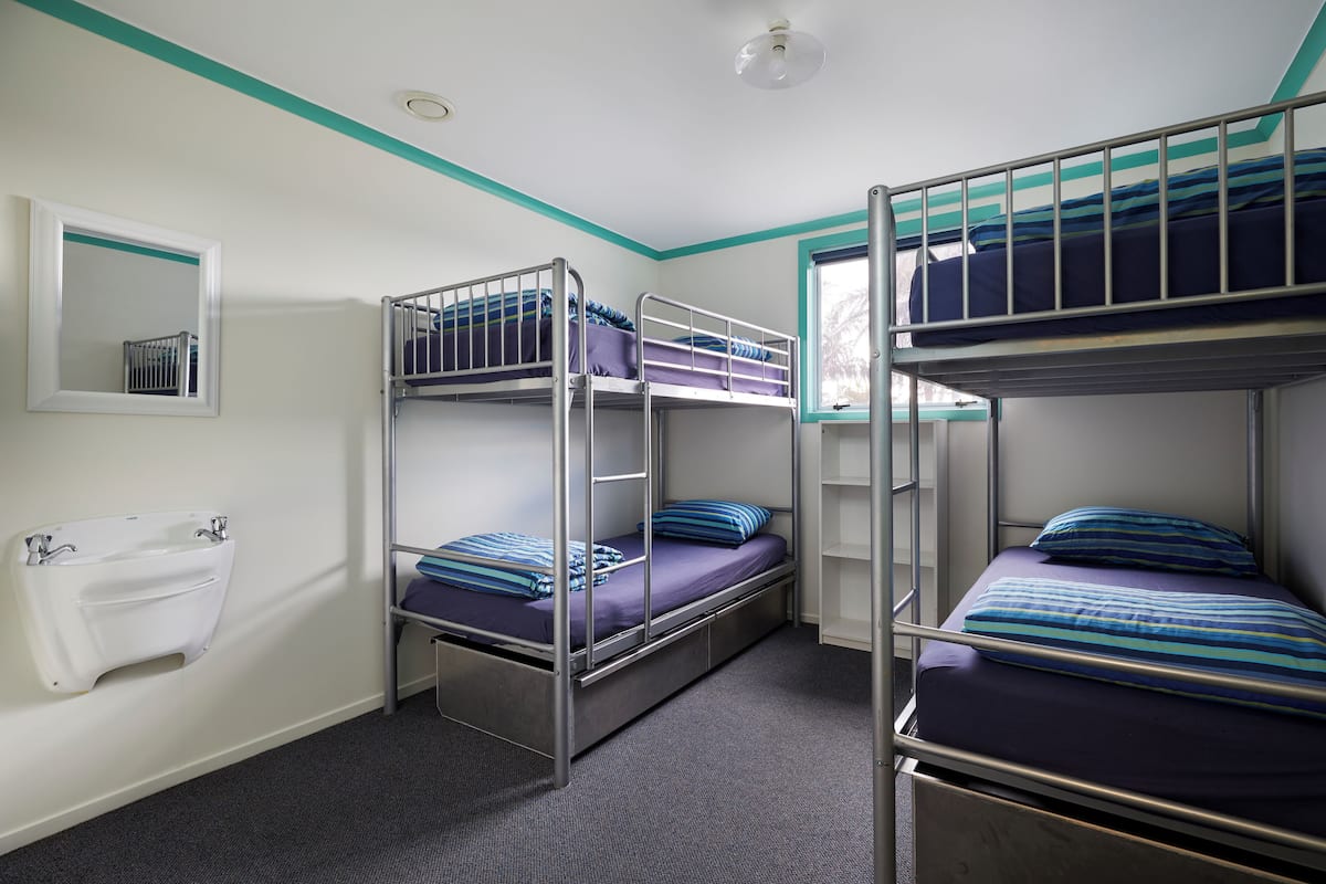 A dormitory room with bunk beds, a window, a mirror, and a towel rack.