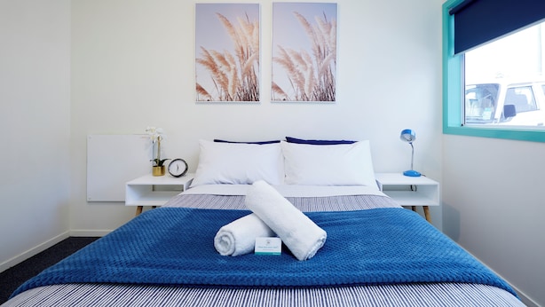 A hotel room with a bed, two bedside tables, a window, and two wall-mounted pictures. - Pacific Coast Lodge and Backpackers (Tauranga)