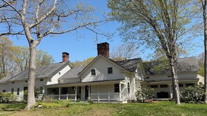 Ein geräumiges, eingeschossiges Haus mit Veranda und Schornstein, umgeben von Bäumen und Gras.