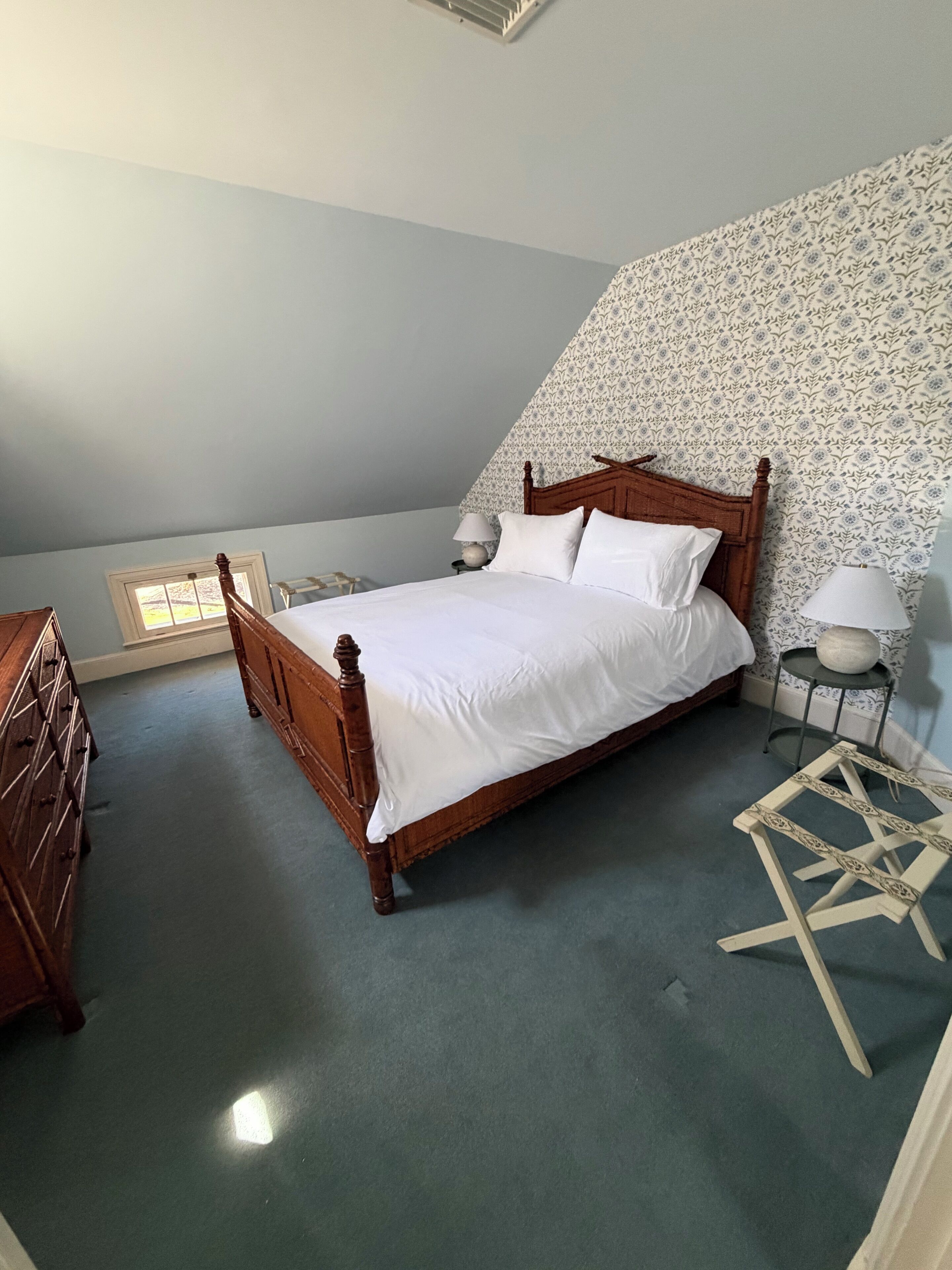 Une chambre à coucher avec un lit en bois, une commode, une petite table avec une lampe et un papier peint à motifs.