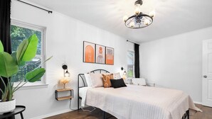 Een slaapkamer met een bed, nachtkastje, lamp en een groot raam met uitzicht.