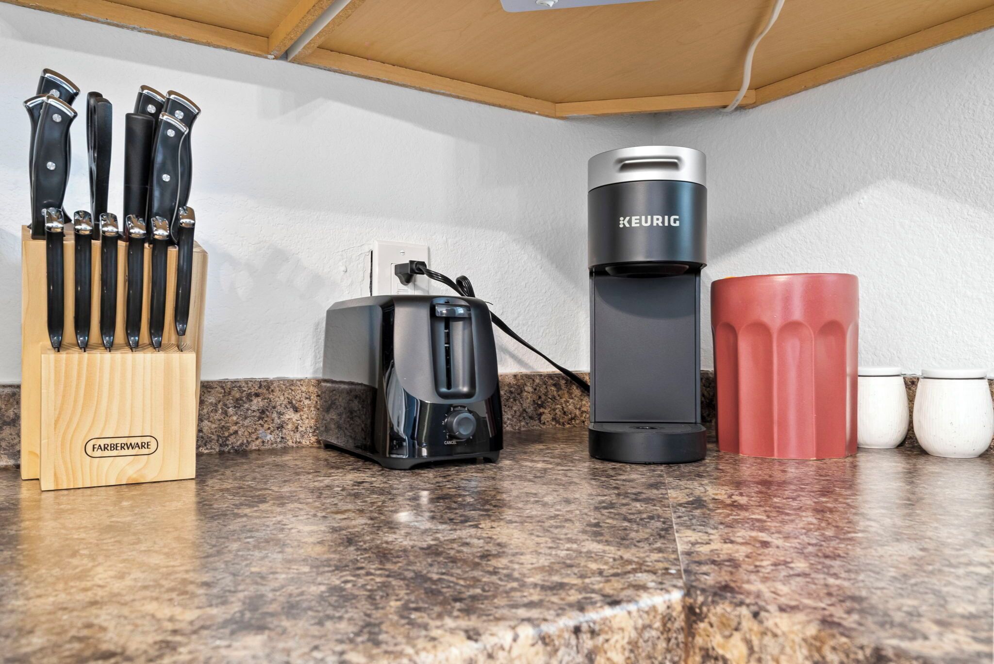 A kitchen counter with a coffee maker, a toaster, a knife block, and a red mug.