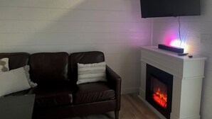 Uma sala de estar com lareira, um sofá e uma televisão na parede.